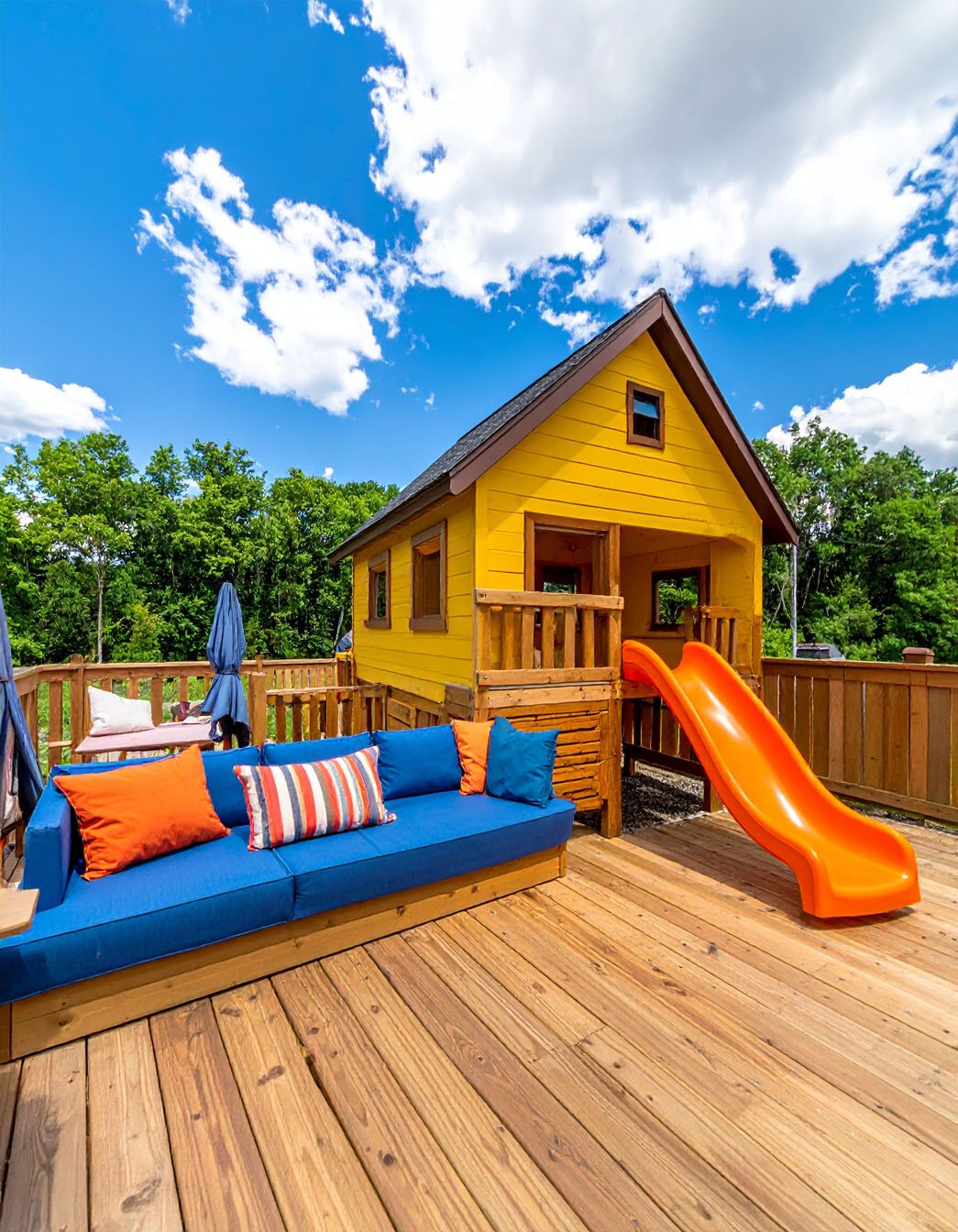 Terrasse en bois avec cabane de jeu jaune, toboggan orange et canapé bleu