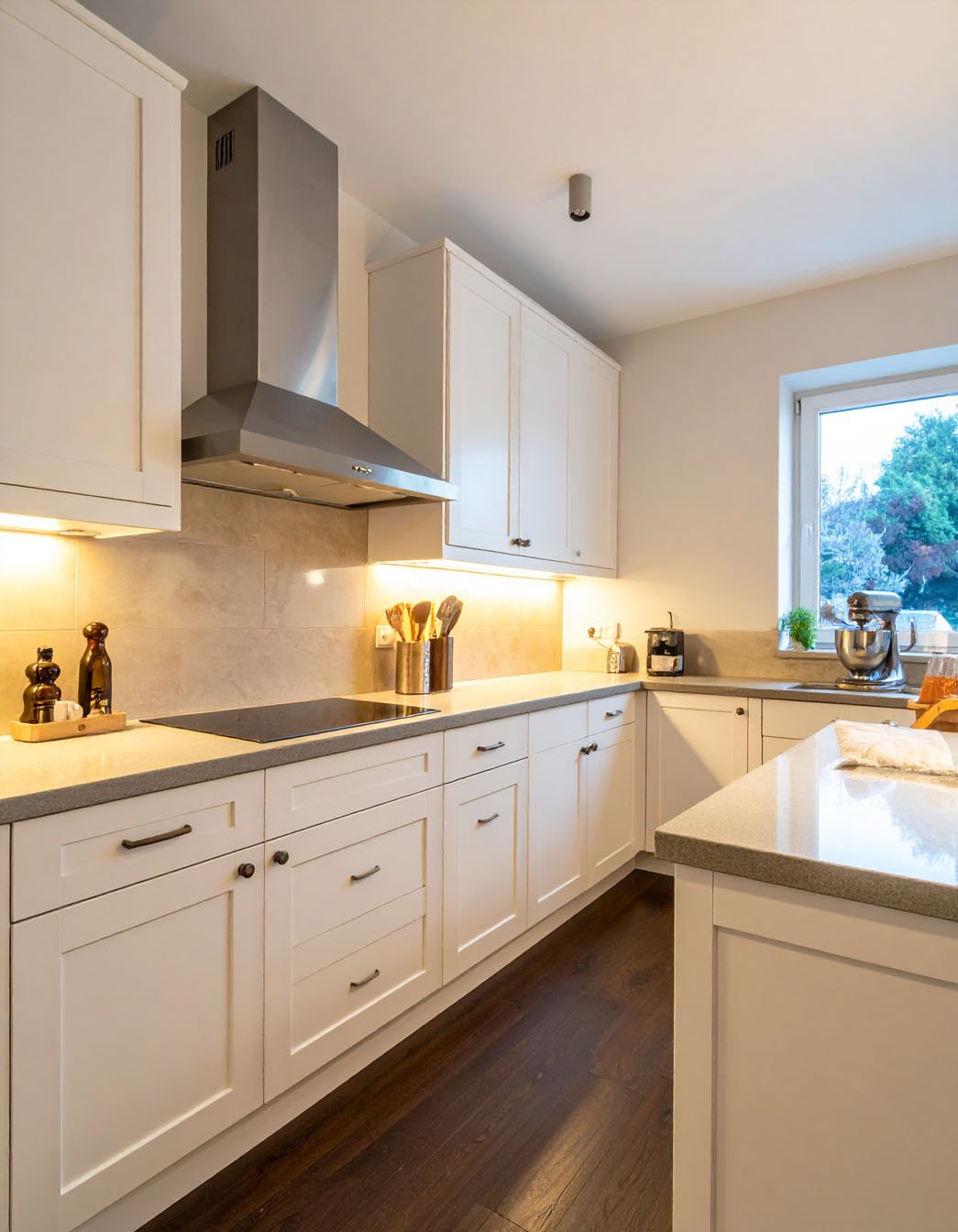 Cuisine avec meubles blancs, plans de travail gris clair et parquet foncé