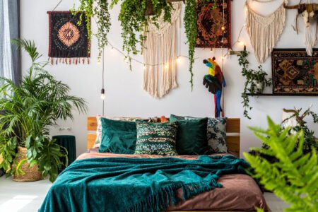 Chambre bohème avec lit en bois, tentures murales, et une profusion de plantes suspendues et au sol