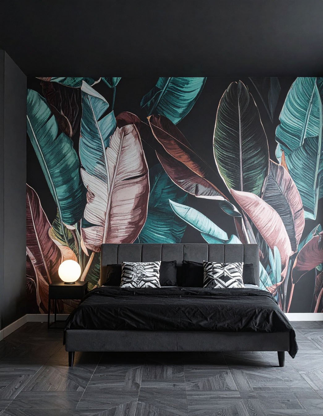 Chambre sombre avec lit noir, et grand papier peint panoramique à motif de feuilles tropicales