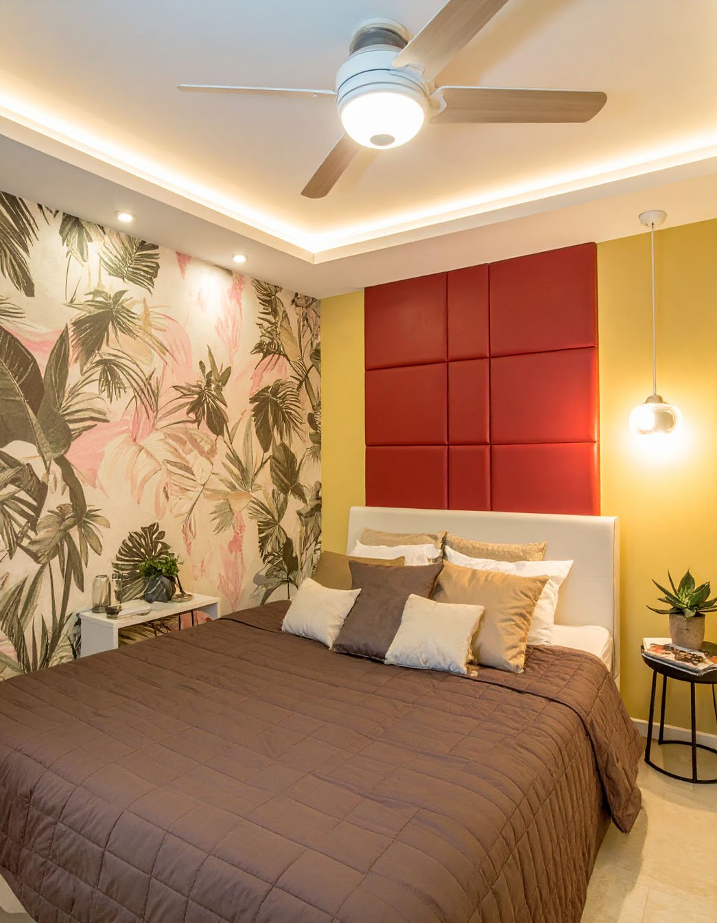 Chambre avec couvre-lit marron, tête de lit rouge et mur jaune, et papier peint à motif tropical
