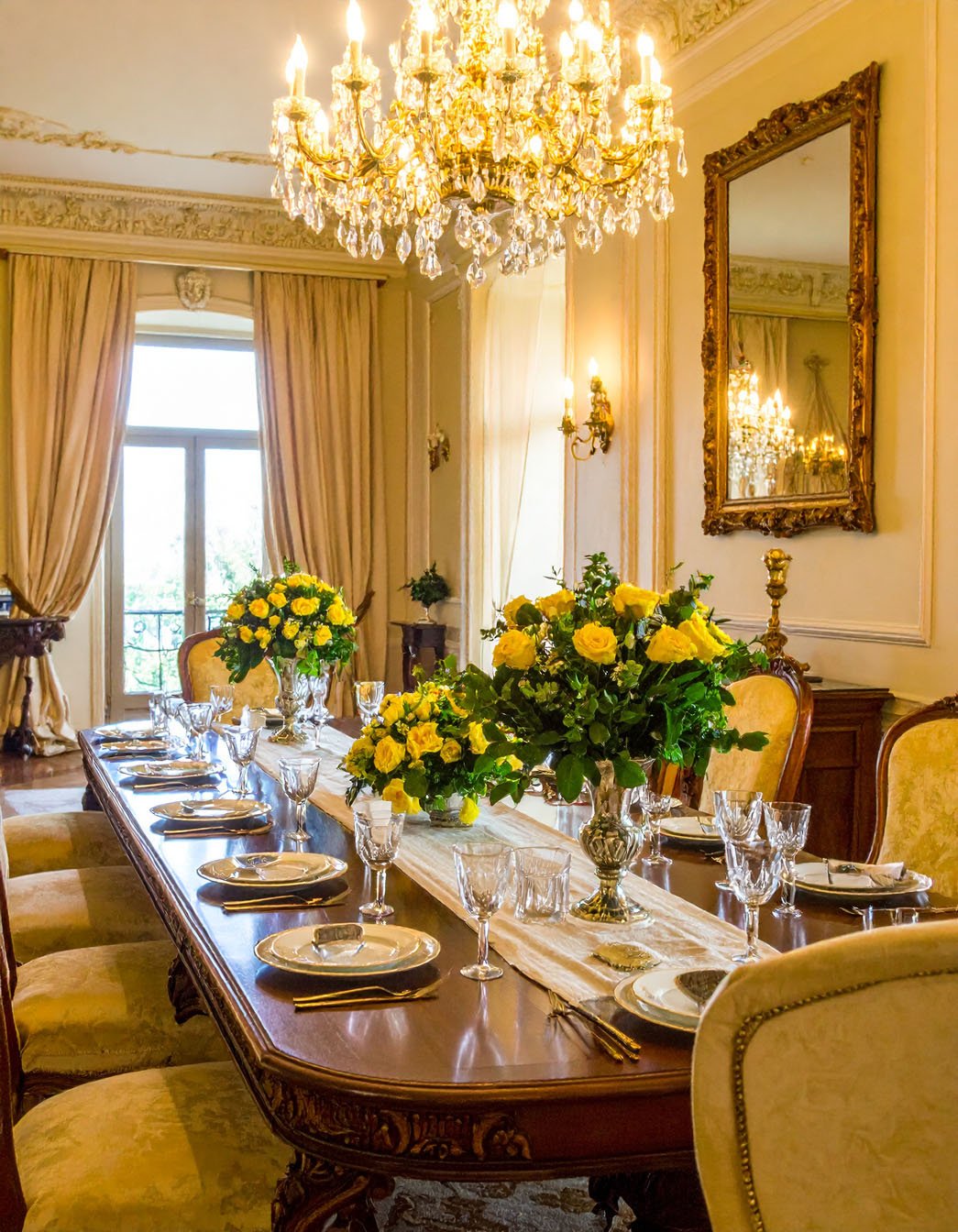Salle à manger classique avec longue table dressée, chaises rembourrées et bouquets de roses jaunes