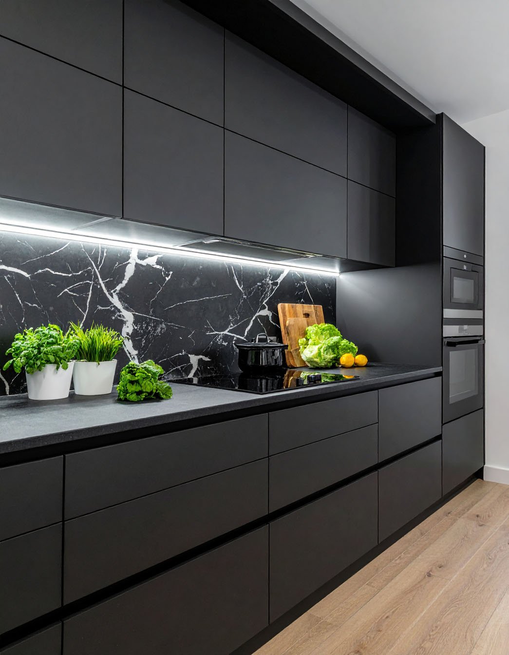 Cuisine minimaliste noire avec crédence effet marbre noir et éclairage linéaire