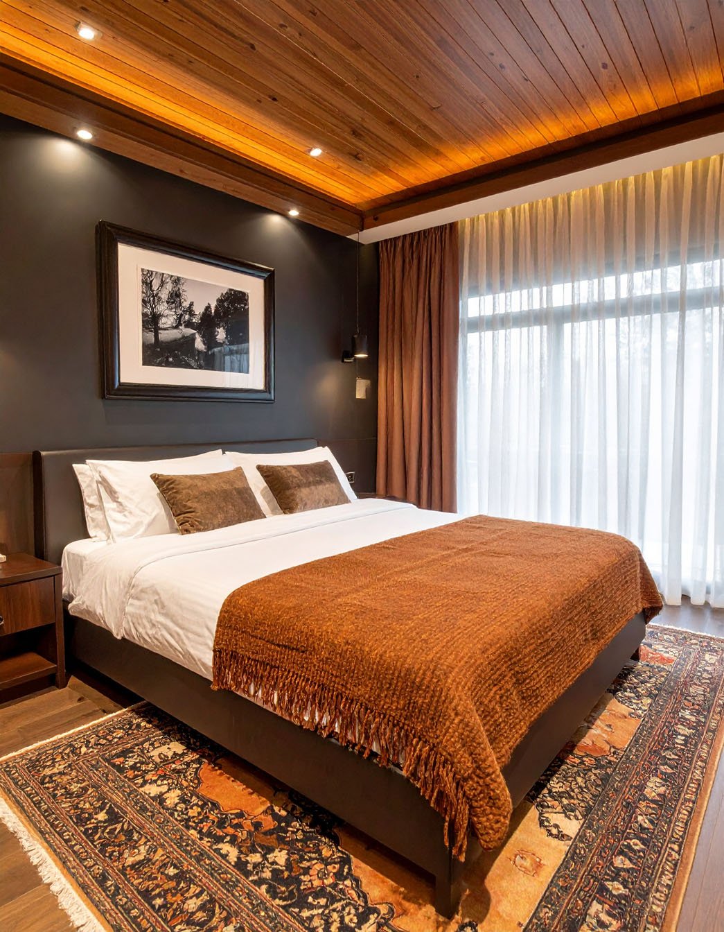 Chambre avec murs foncés, plafond en lattes de bois, plaid couleur rouille et tapis persan