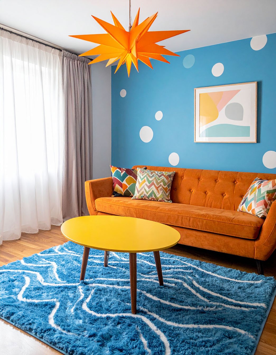 Salon coloré avec canapé orange, table basse jaune, tapis bleu et mur à pois