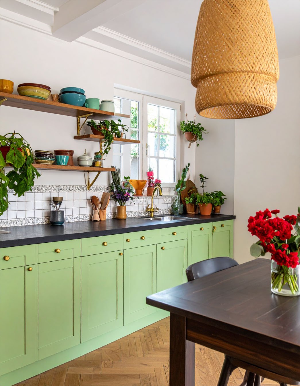 Cuisine avec meubles bas vert clair, étagères en bois, plantes et suspension en rotin