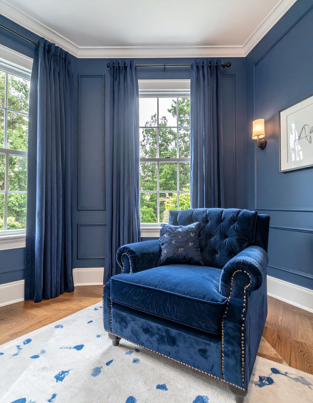Salon avec murs gris, fauteuil en velours bleu capitonné et table d'appoint dorée