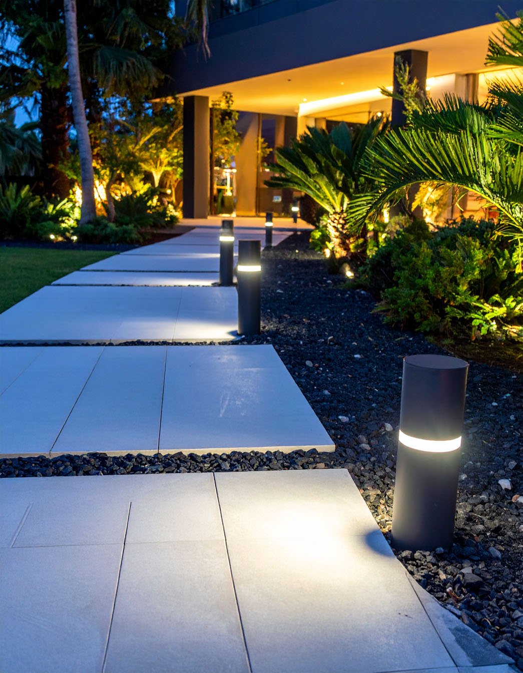 Allée de jardin moderne éclairée par des bornes lumineuses noires le long d'un mur en crépi