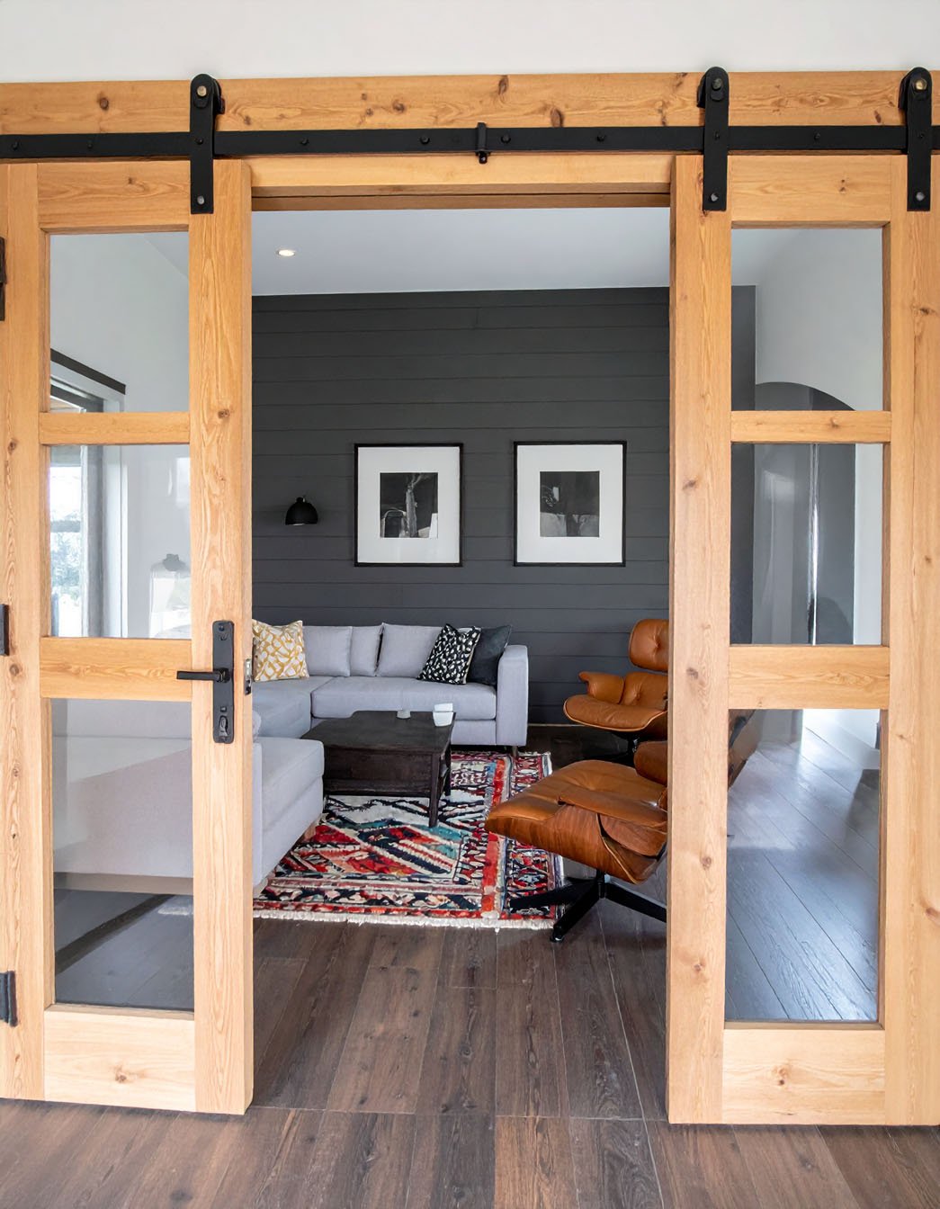 Vue à travers des portes coulissantes en bois vitrées sur un salon avec canapé gris et fauteuil en cuir