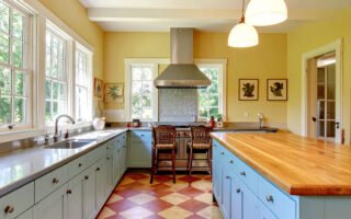 Cuisine avec meubles bleu pastel, îlot avec plan de travail en bois et sol à damier terre cuite