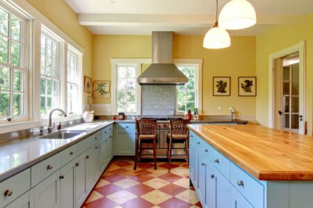 Cuisine avec meubles bleu pastel, îlot avec plan de travail en bois et sol à damier terre cuite