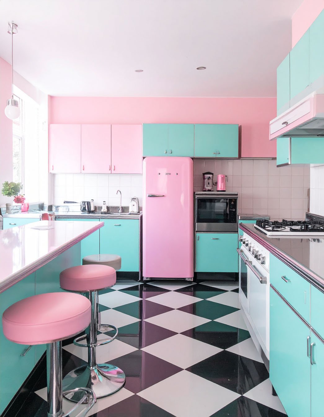 Cuisine rétro rose et turquoise avec îlot, tabourets roses et sol à damier