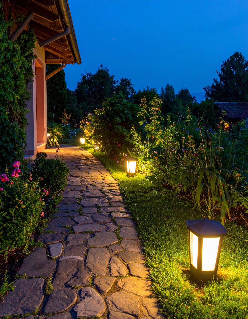 Allée de jardin en dalles éclairée par des bornes lumineuses au crépuscule