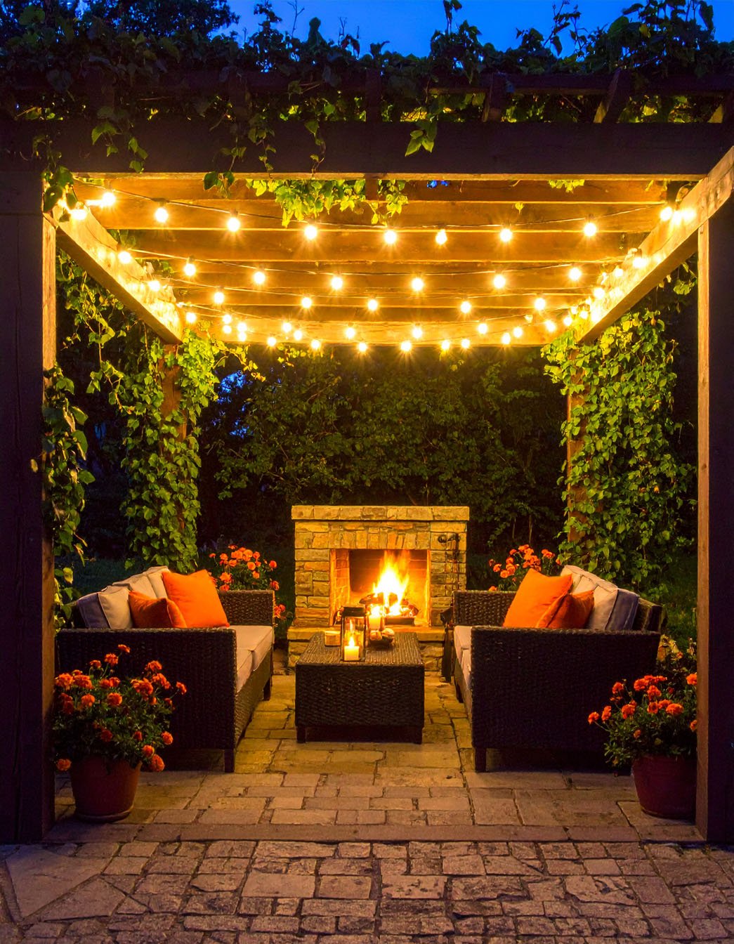 Terrasse de soirée avec pergola illuminée, salon de jardin et foyer en pierre allumé