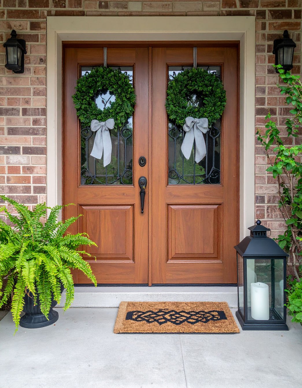 Double porte d'entrée en bois avec vitres décoratives, deux couronnes et une lanterne