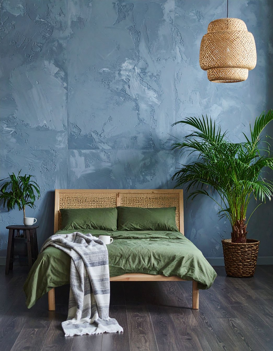 Chambre avec mur texturé bleu-gris, lit en bois avec literie vert olive et grande plante