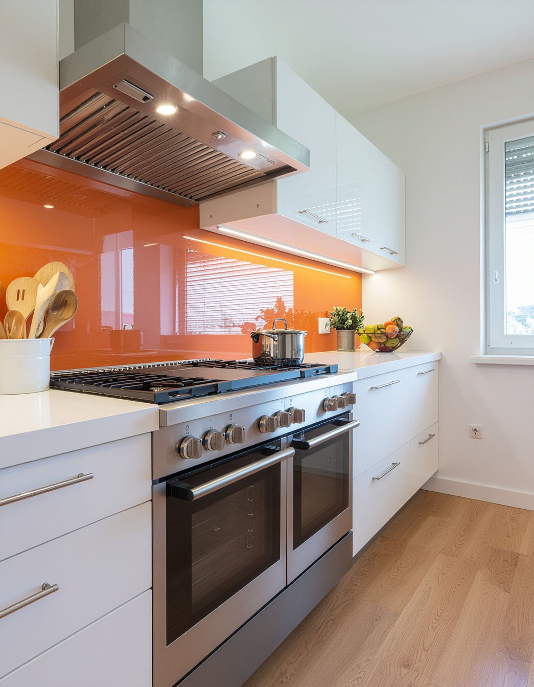 Cuisine avec meubles blancs, crédence en verre orange vif et grand piano de cuisson inox
