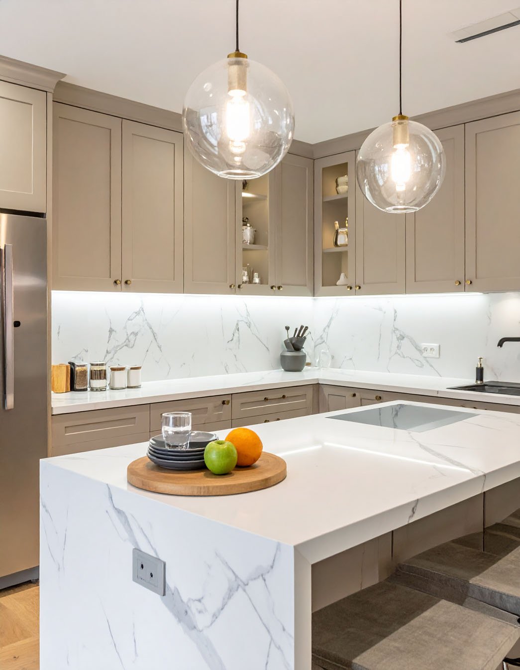 Cuisine avec meubles taupe, îlot effet marbre blanc et suspensions globes transparentes