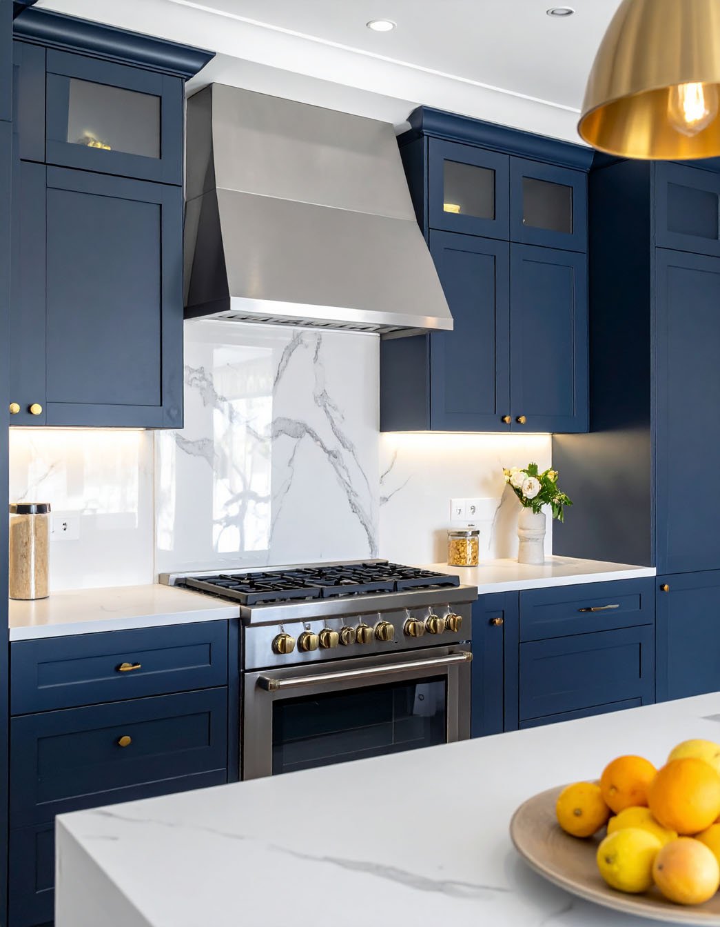 Cuisine bleu marine avec crédence en marbre blanc, hotte inox et grande suspension dorée