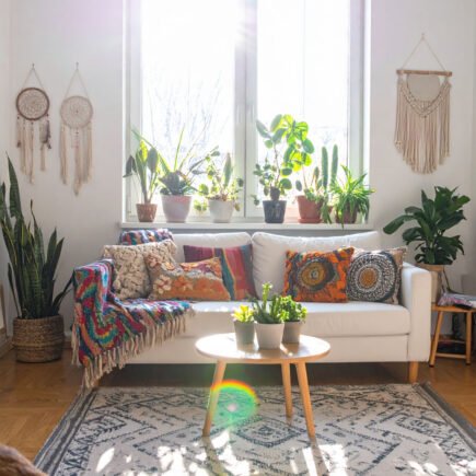 Salon bohème lumineux avec canapé blanc, coussins colorés, plantes et attrape-rêves