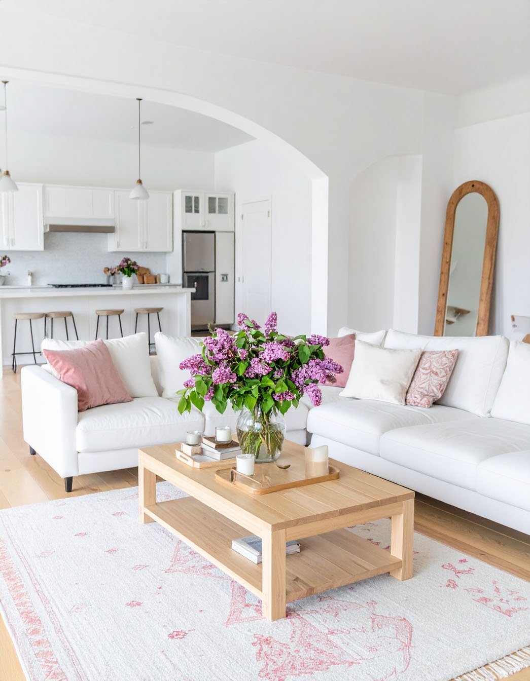 Salon ouvert et lumineux avec canapés blancs, bouquet de lilas et tapis à motifs discrets