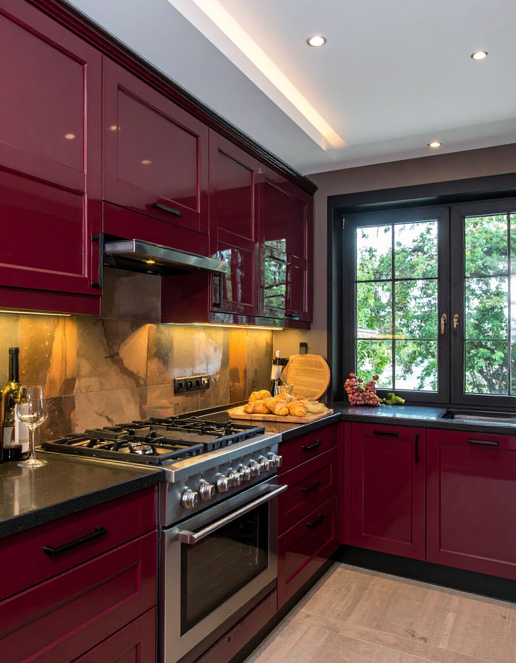 Cuisine avec meubles rouge bordeaux laqué, plans de travail noirs et piano de cuisson inox