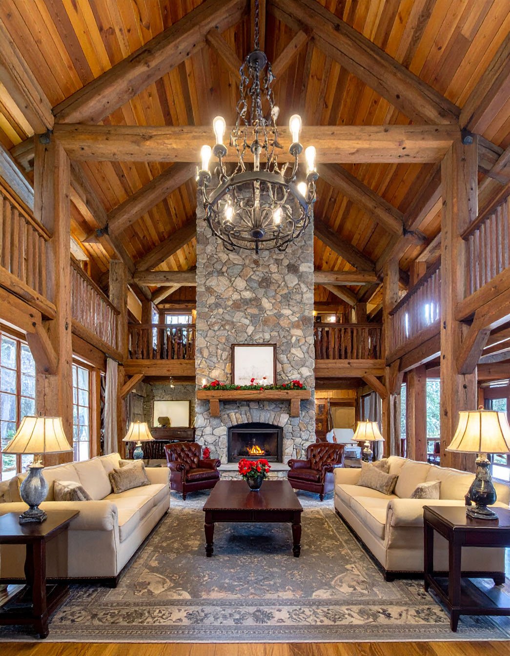 Grand salon de chalet en bois avec cheminée en pierre imposante et lustre rustique