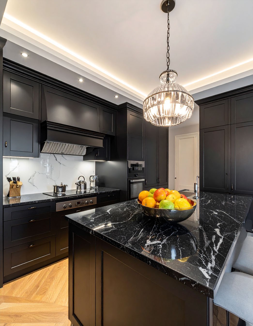 Cuisine noire avec îlot et plans de travail en marbre noir, et lustre en cristal