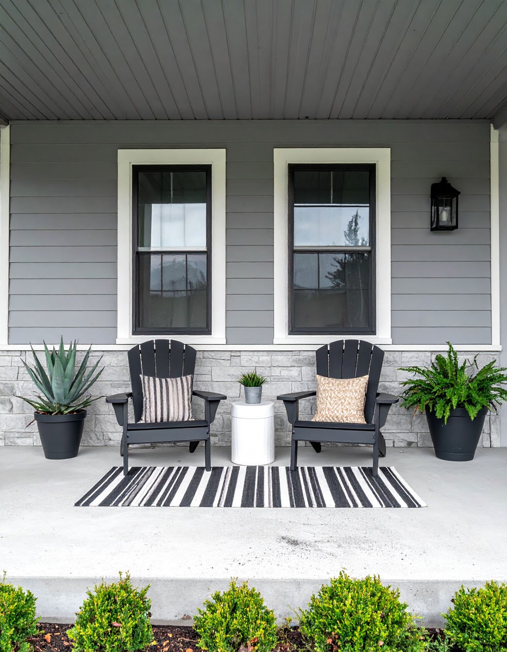Porche moderne avec deux fauteuils Adirondack noirs, tapis rayé, plantes en pots