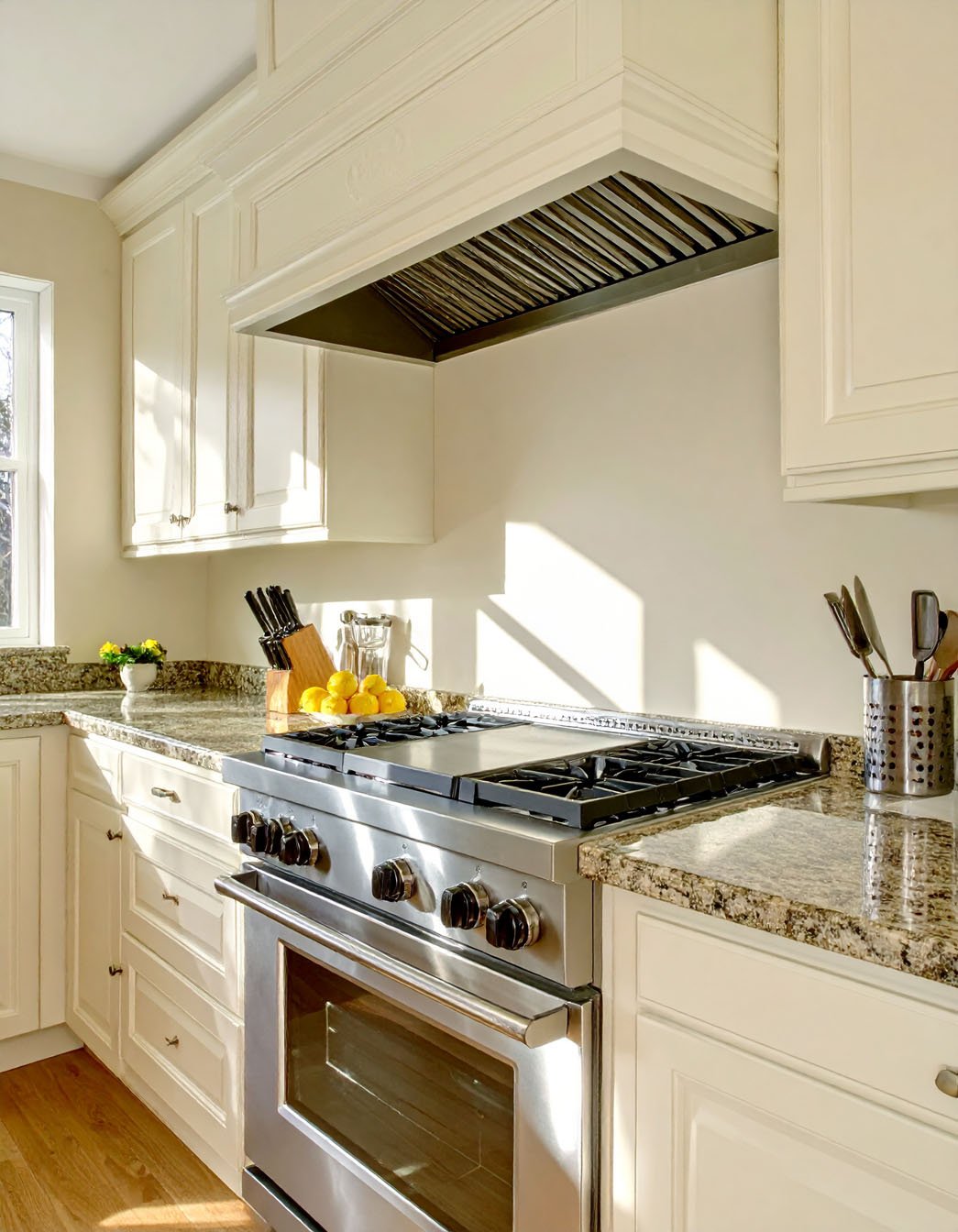 Cuisine avec meubles blanc cassé, plans de travail en granit et piano de cuisson inox