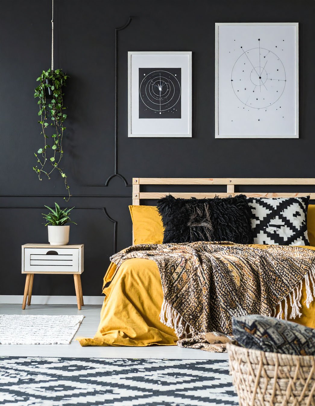 Chambre avec murs noirs à moulures, lit avec literie moutarde et coussins à motifs graphiques