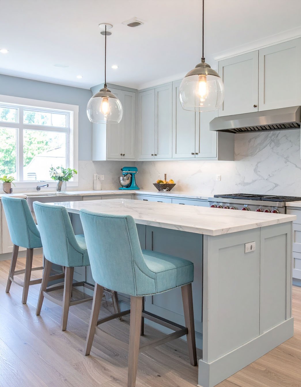 Cuisine avec îlot bleu-gris clair, tabourets en tissu turquoise et suspensions globes en verre