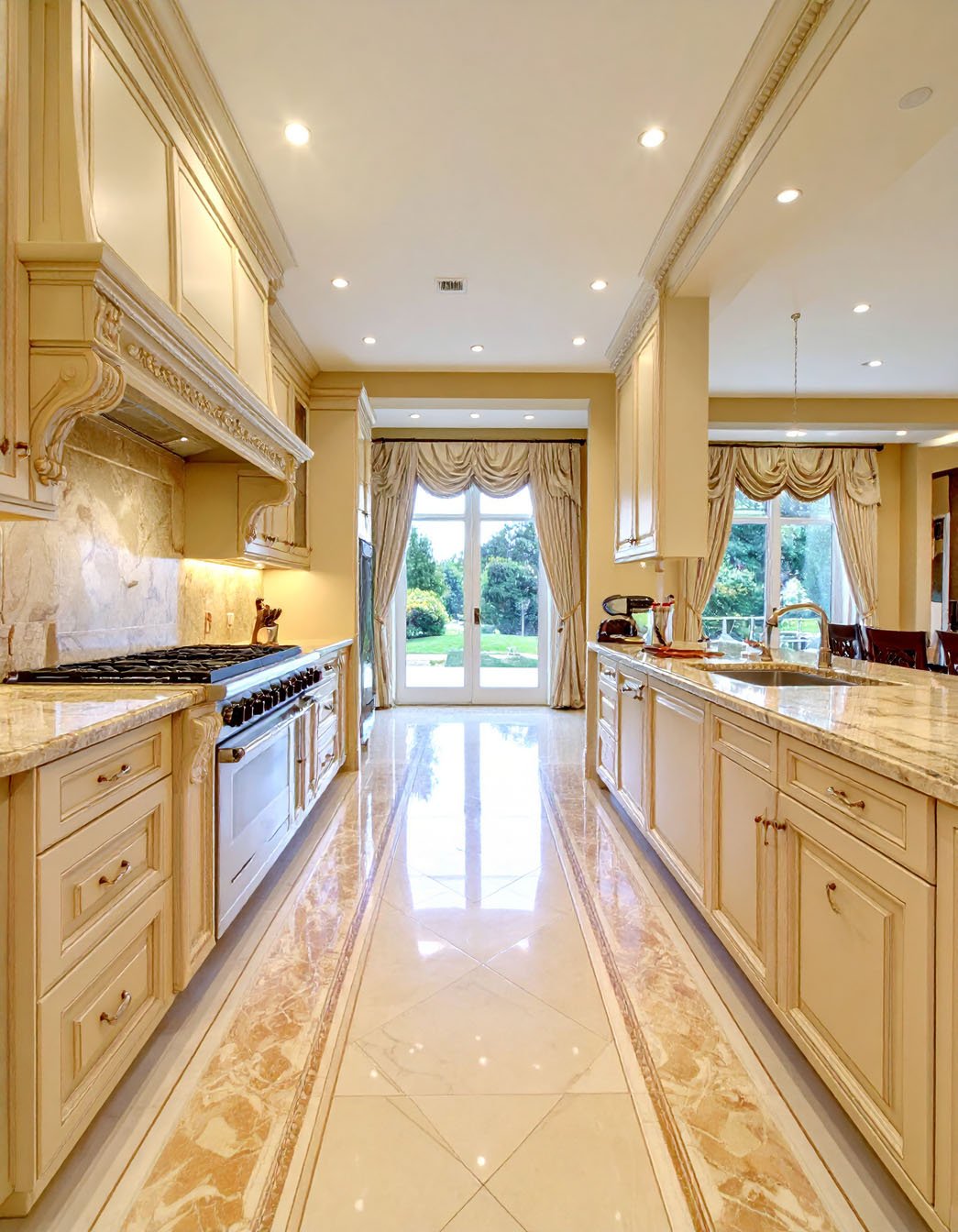 Cuisine de luxe couleur crème avec sol en marbre à motifs et vue sur jardin