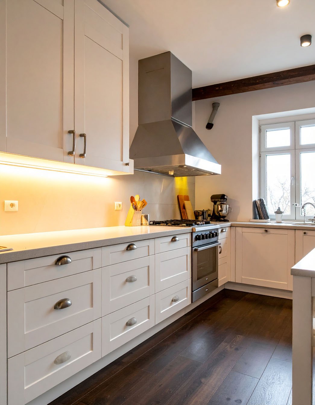 Cuisine avec meubles blancs, hotte en inox, parquet foncé et poutre apparente