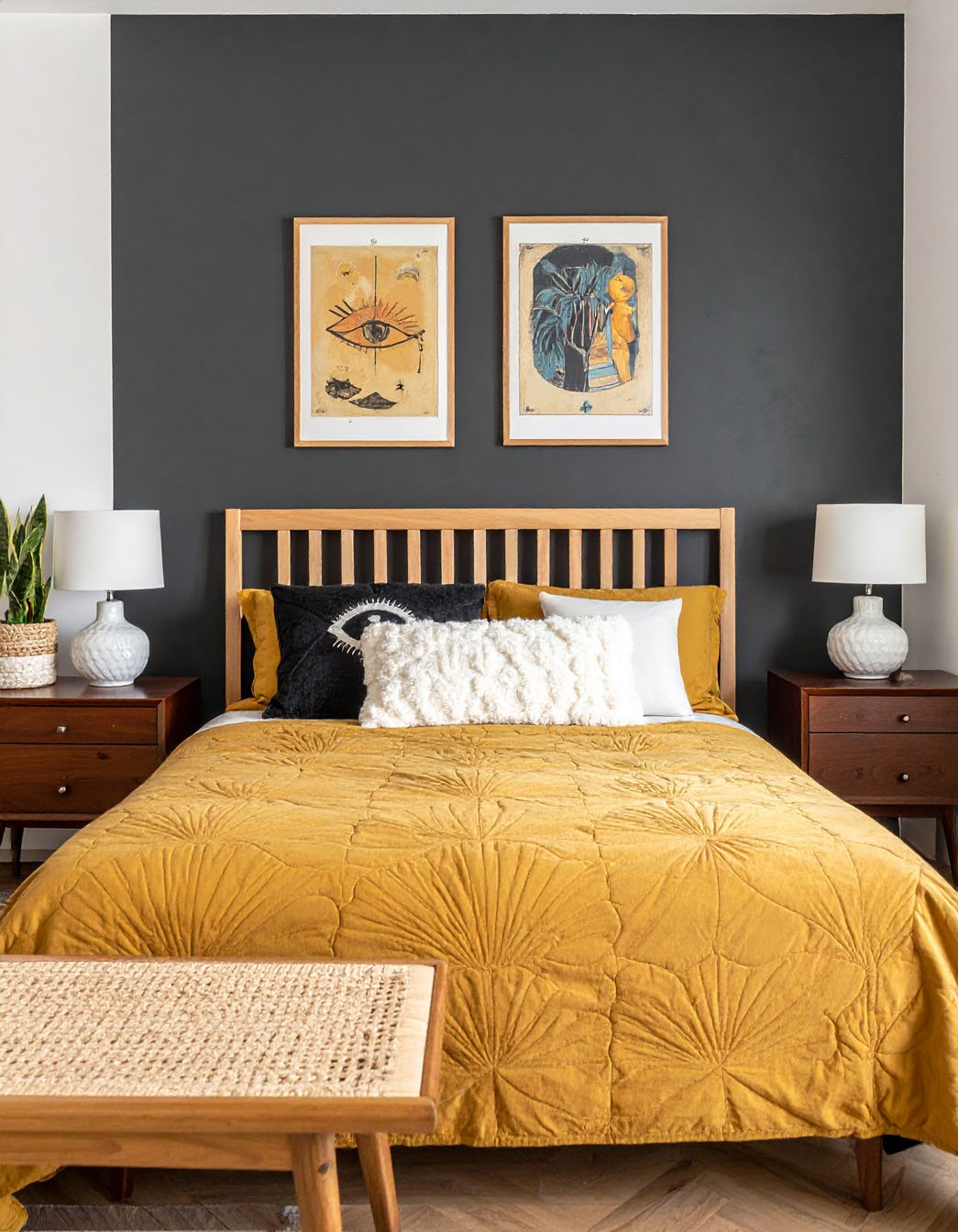 Chambre avec mur gris foncé, lit en bois clair, couvre-lit moutarde et tableaux mystiques