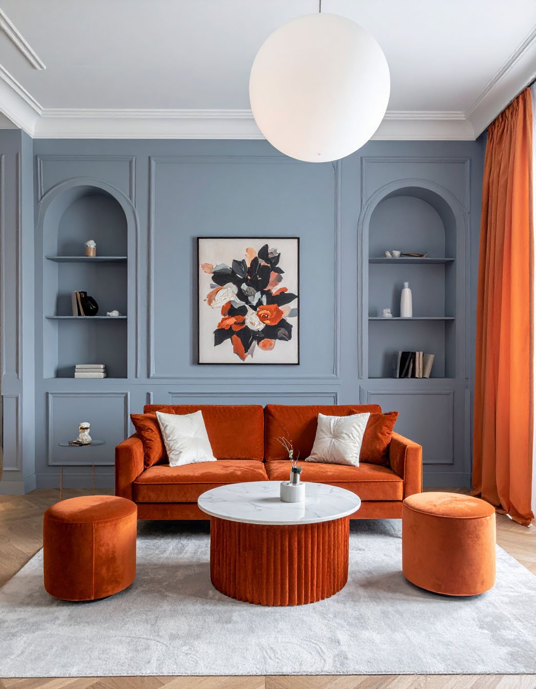 Salon avec murs bleu-gris à niches, canapé et poufs en velours orange brûlé, table basse assortie