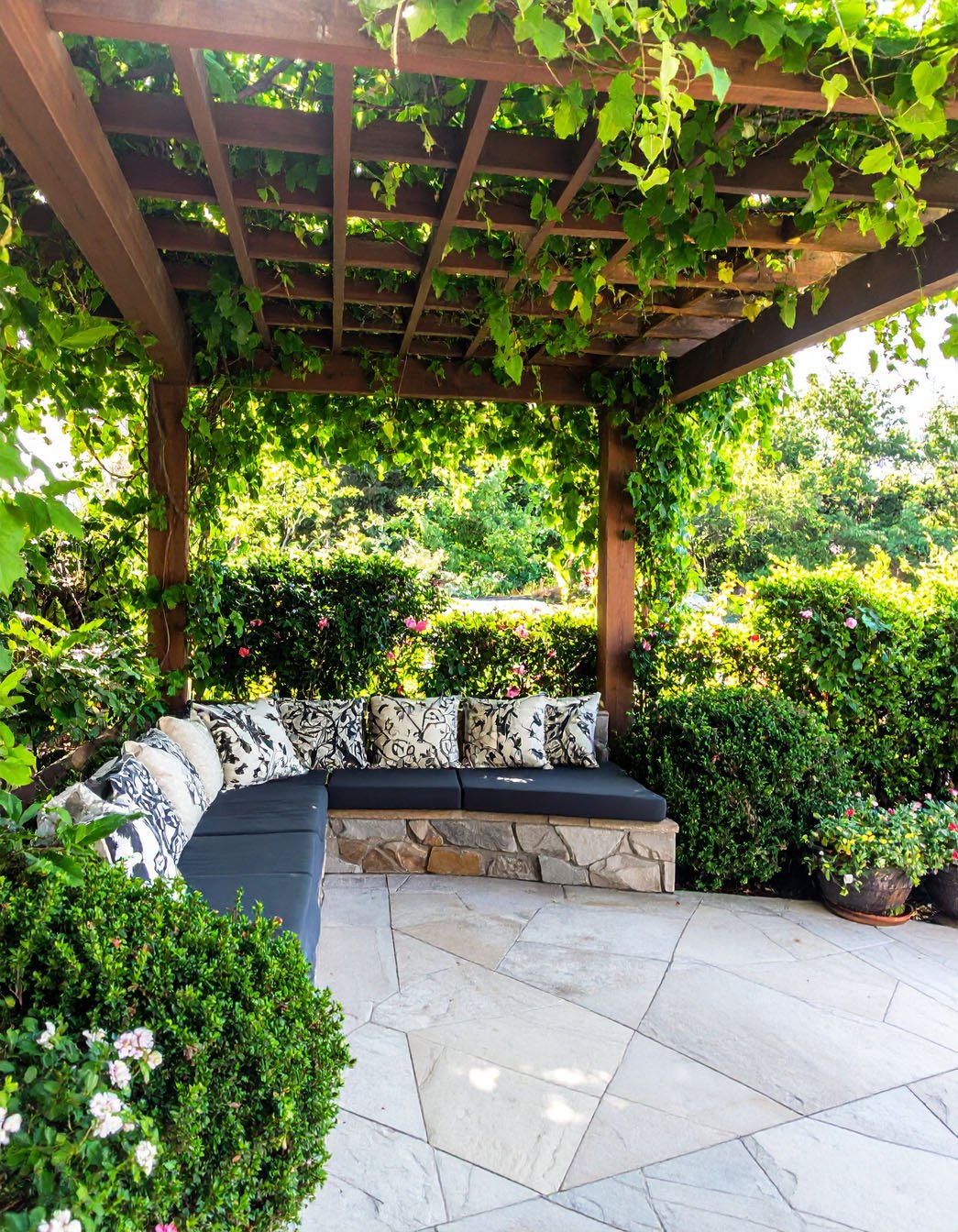 Banquette d'angle confortable sous une pergola recouverte de vigne vierge