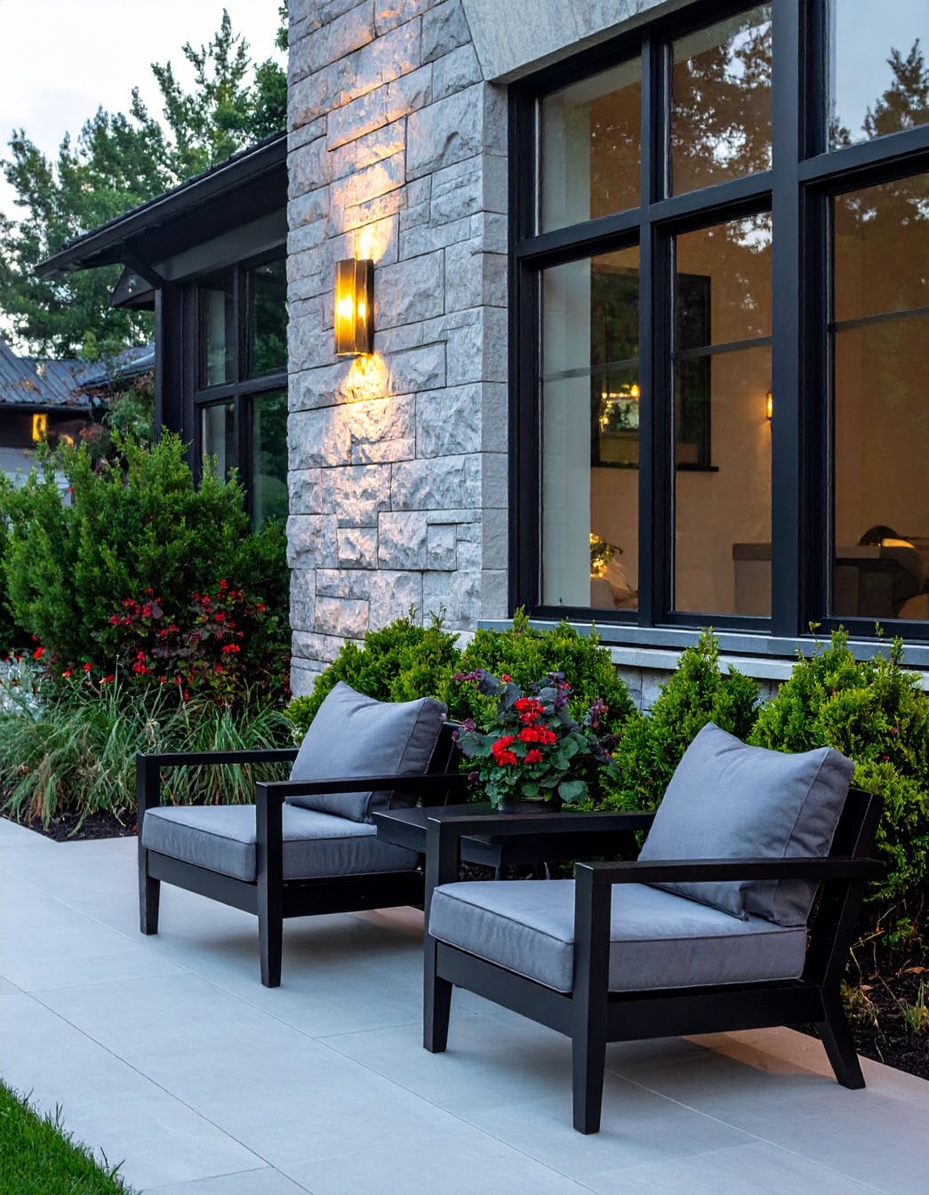 Terrasse moderne avec fauteuils noirs à coussins gris et mur en pierres