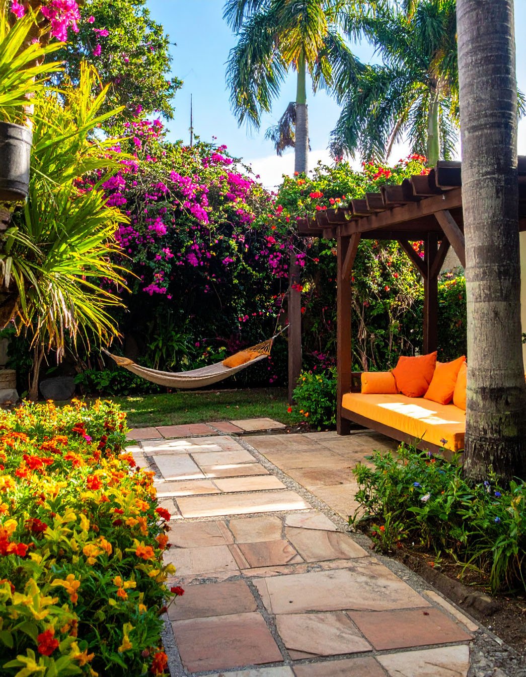 Jardin tropical avec allée en dalles, hamac et banquette à coussins orange