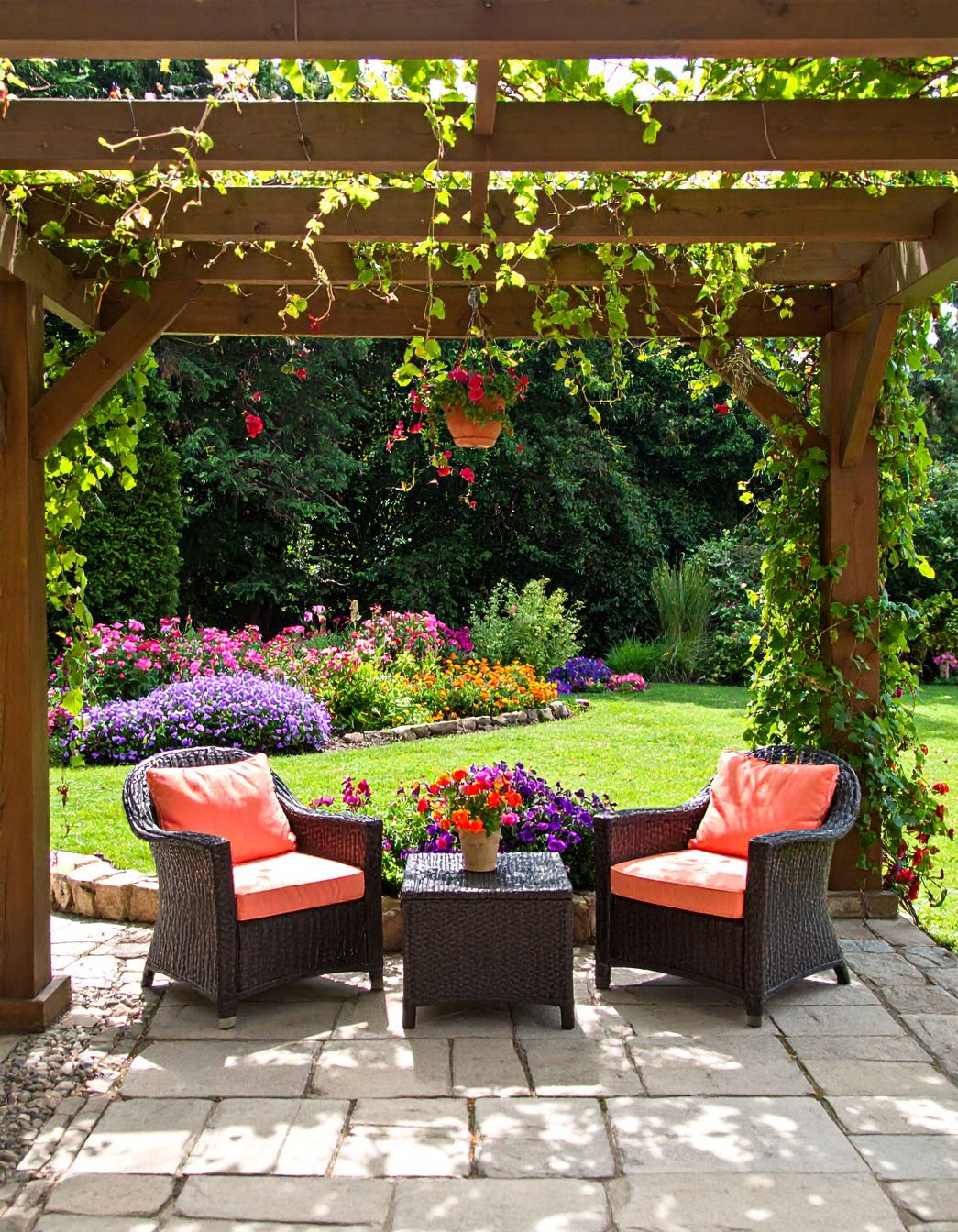Salon de jardin en résine tressée sous une pergola fleurie avec vue sur un parterre coloré