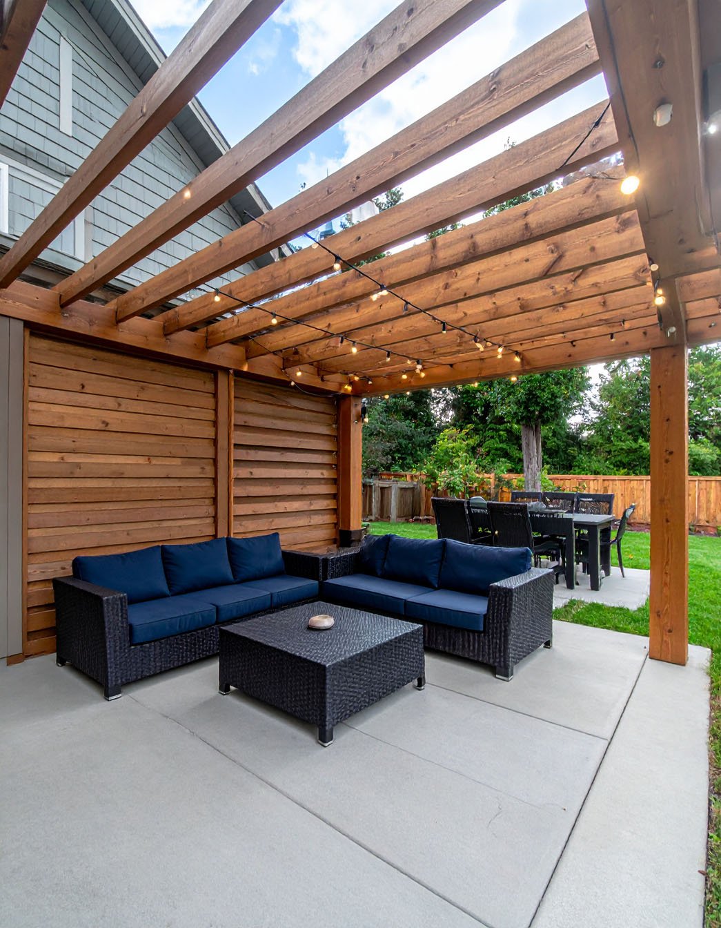 Terrasse en dalles avec pergola en bois, salon de jardin et barbecue