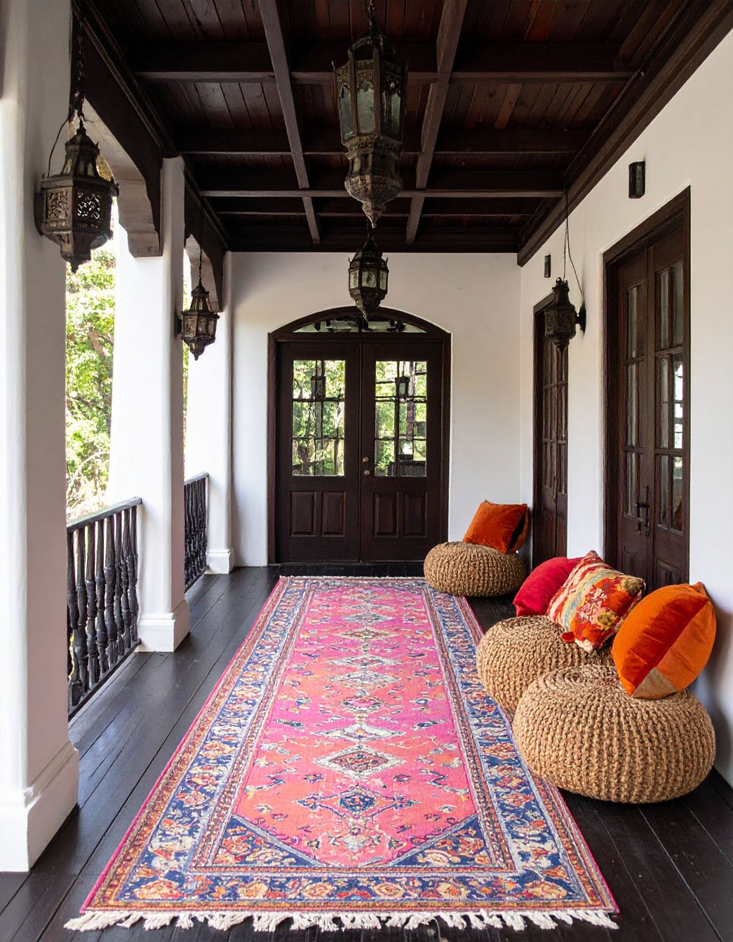 Porche de style marocain avec tapis rose vif, poufs en jute et lanternes suspendues
