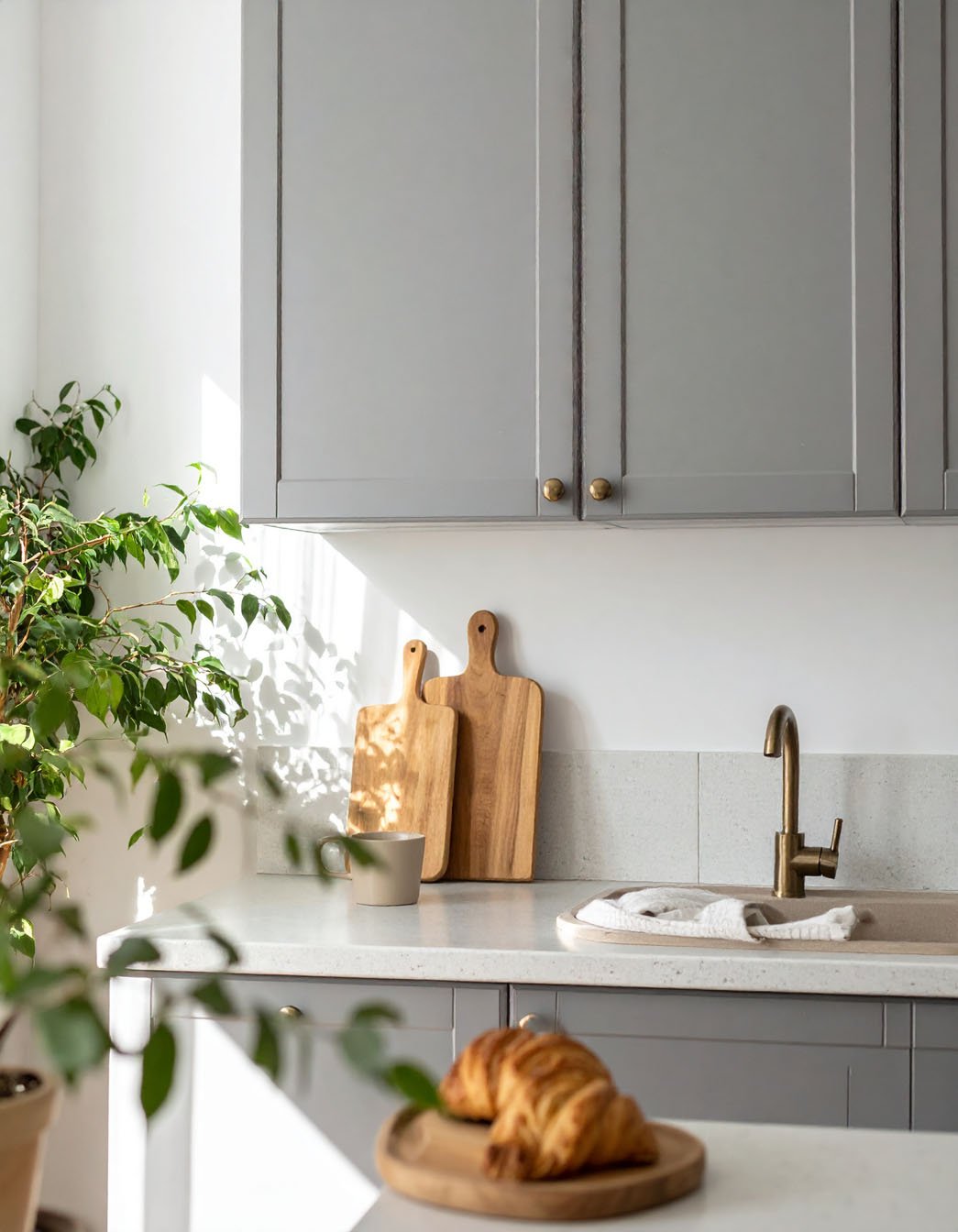 Cuisine avec meubles gris, planches à découper en bois et croissant au premier plan