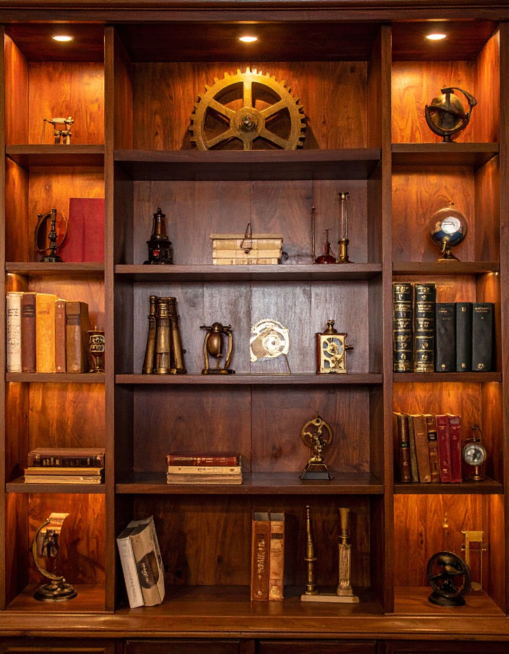 Bibliothèque en bois foncé avec étagères éclairées exposant des instruments scientifiques anciens et des livres