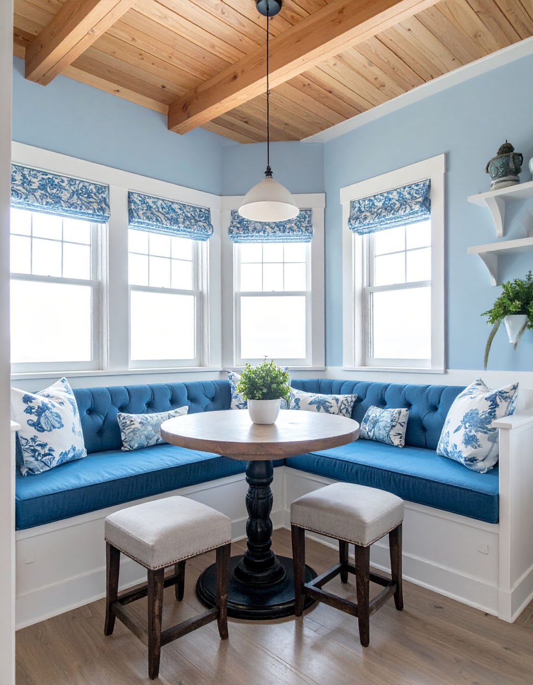 Coin repas d'angle avec banquette capitonnée bleue, coussins à motifs floraux et plafond en bois