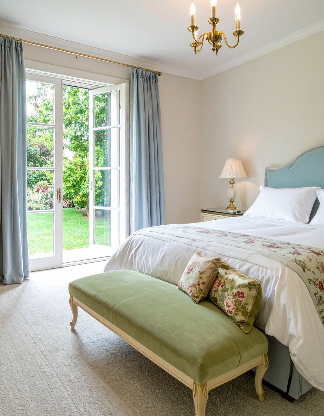 Chambre élégante avec lit à tête de lit bleu ciel, banc vert olive et portes-fenêtres