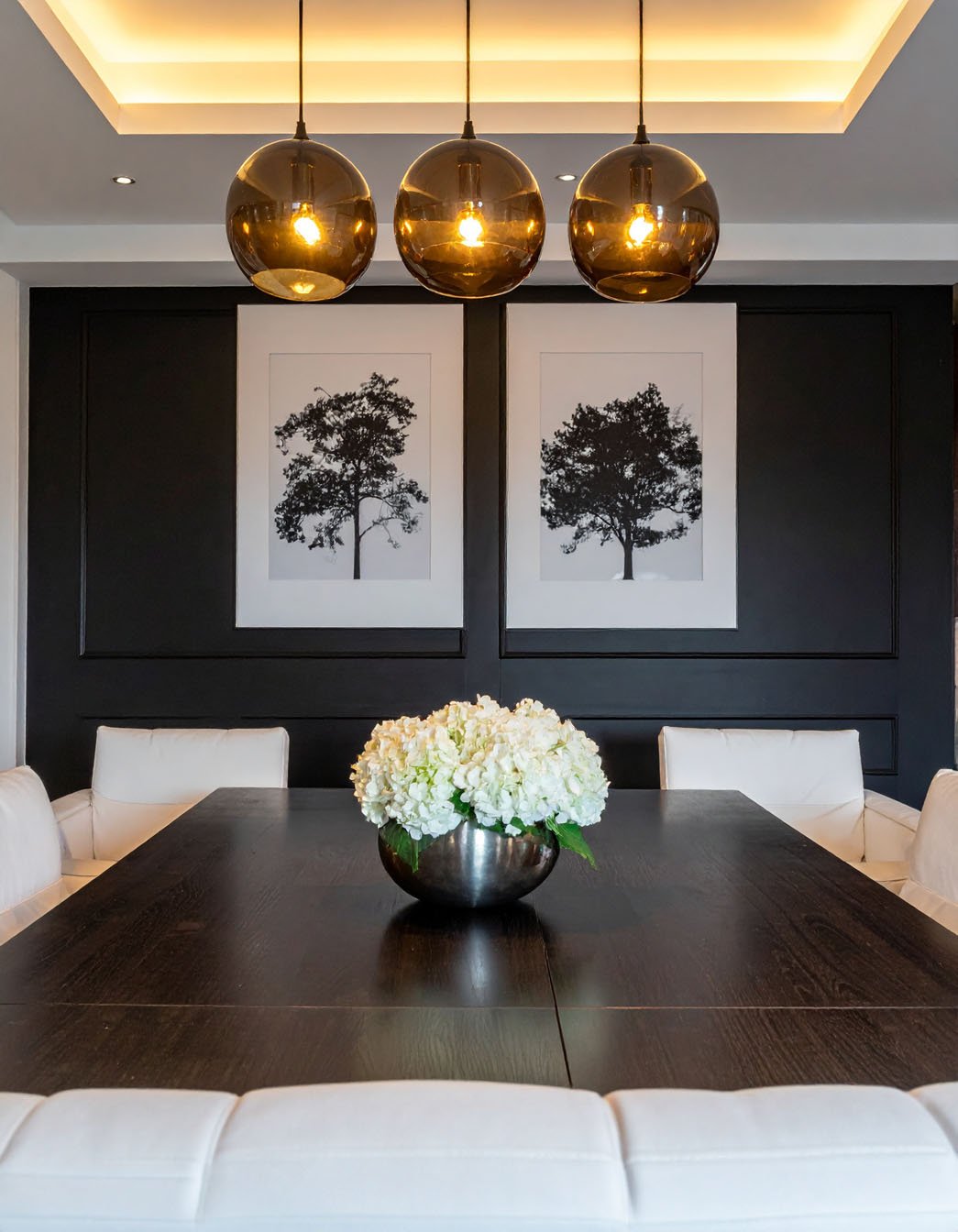 Salle à manger avec mur noir, table foncée, chaises blanches et suspensions globes ambrées