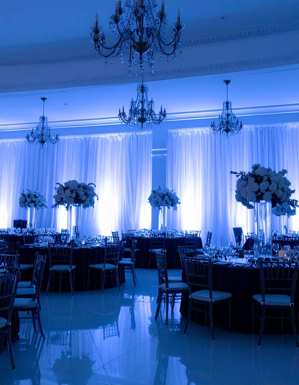 Salle de réception élégante avec tables dressées, éclairage bleu et grands arrangements floraux