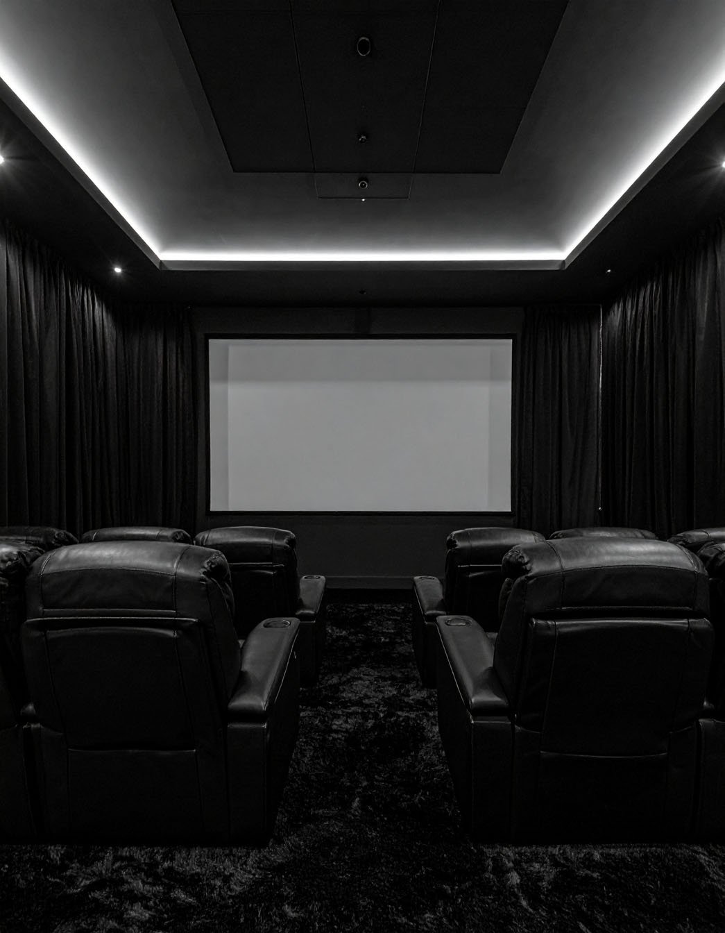 Salle de cinéma privée sombre avec fauteuils en cuir noir et grand écran