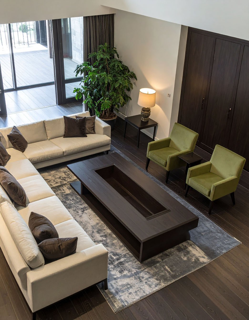 Salon spacieux avec grand canapé d'angle beige, fauteuils verts et table basse avec foyer intégré, vue de dessus